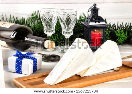 Brie cheese, a bottle of wine, coniferous green branches on a wooden background. Goodies for the holiday. The concept of Christmas and the New year. Toned