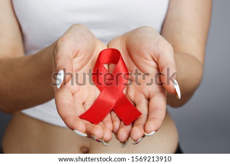female hands holding red AIDS awareness ribbon, healthcare and medicine concept