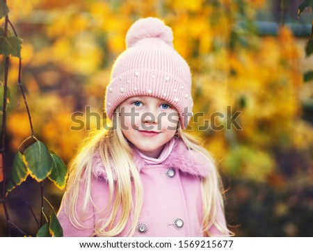Portrait of beautiful little girl in pink hat and coat in autumn park 