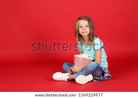 Young girl with popcorn in bucket sitting on red background