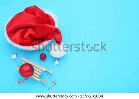 Red santa hat with christmas ornaments and wooden sleigh on blue background