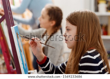 Little artist drawing on canvas. Girl holding a brush and making strokes. Art workshop for children.