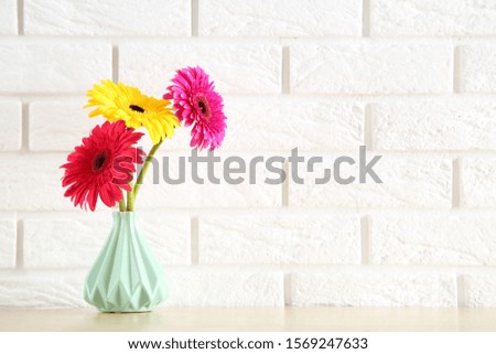 Ceramic vase with gerbera flowers on white brick wall background