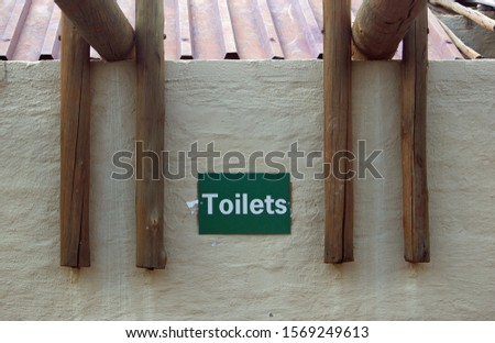 White paint on green metallic plate with word Toilets against  wall indicating location of toilets