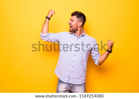 Young man in glasses holding hands fists up celebrating success on orange yelllow background.