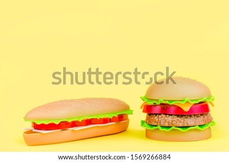 fast food. plastic hamburger, hot dog on a yellow background.