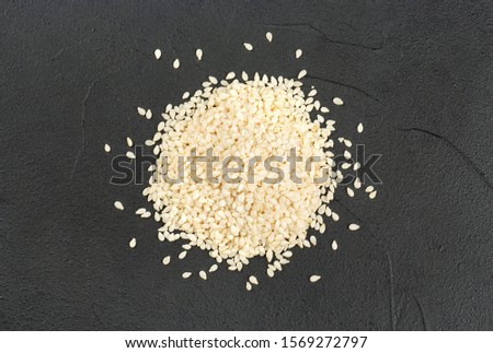 Pile of white sesame seeds on a dark concrete background, top view