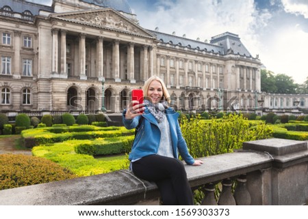 Young woman posing against the backdrop of the Royal Palace in Brussels and taking pictures on her phone, Belgium