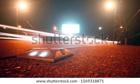 Roadside ground signalization light with traffic lights streaks of passing by vehicles in the background