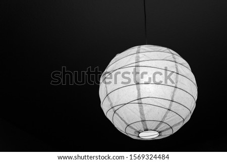 Black and white tone of sphere pendent lamp lantern with incandescent light bulb and translucent paper material, in dim dark interior ceiling room.