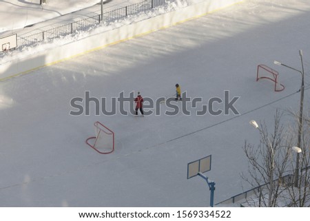 mom and son play hockey on an empty ice rink, top view