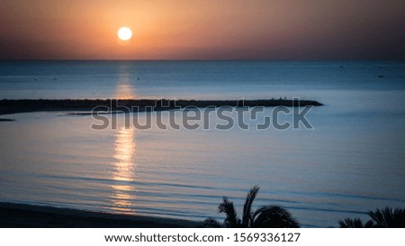 Aerial view of the sun rising over the Mediterranean Sea. The calm water reflects the sunlight like a mirror. The photo was taken in Punta Negra in the town of Cullera, Valencia, Spain, Europe 