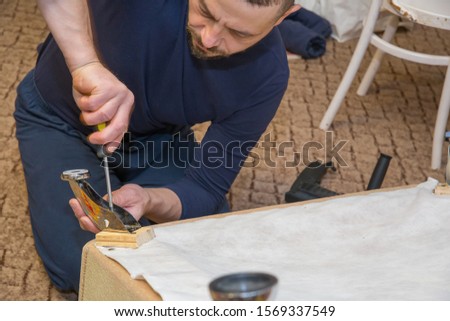 A man holds a screwdriver in his hands and repairs furniture. Photo of real people at work.
