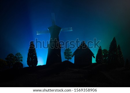 Windmill silhouette standing on hill against the night sky. Night decor with old windmill on hill with horror toned foggy background with light. Horror concept