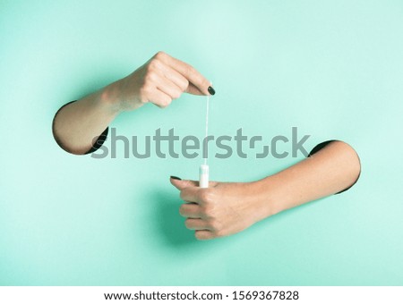 Female hands hold hygienic tampon through a hole on neon mint background.