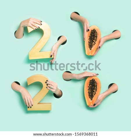 Female hands hold golden new year 2020 digits and papaya through a hole on neon mint background.