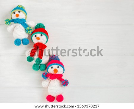 Three Little cute crocheted snowmen in a multicolor hats and scarfs on a white wooden background