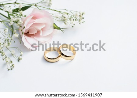 Pink flowers and two golden wedding rings on white background. Royalty-Free Stock Photo #1569411907