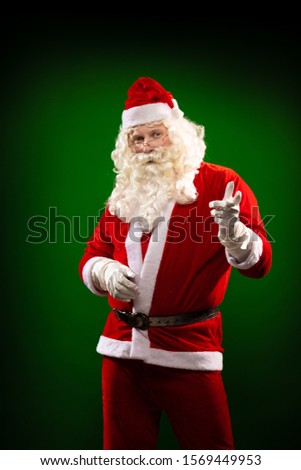 Male actor in a costume of Santa Claus dancing and gesturing, posing on a green background