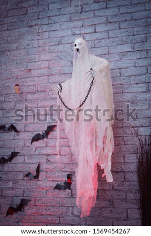 Halloween ghost hanging on the wall with chain on his wrists and bats around