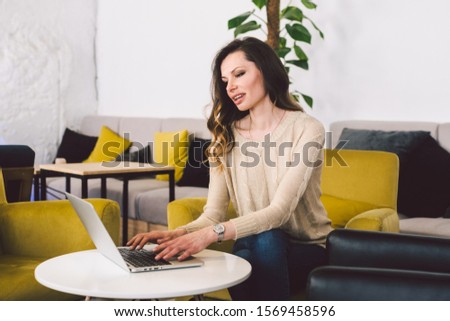 Young middle aged Caucasian woman with long hair. Casual clothes using laptop computer indoors. Cafe restaurant on chair wooden table. Profession freelancer, blogger and writer. Hands typing keyboard.