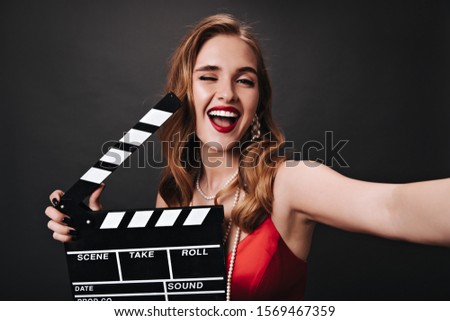 Lady in red top winking, holding clapperboard and taking selfie
