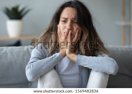 Close up view upset 30s female sitting on couch looking unhappy and desperate concept of betrayal of beloved man, difficult decision about abortion, alcohol or drugs addicted person need clinic rehab Royalty-Free Stock Photo #1569482836