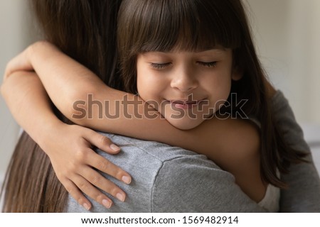 Close up of adorable brown-haired cutie little daughter face with closed eyes cuddle her mother showing sincere love and strong attachment heartfelt moment, new mom for adopted grateful child concept Royalty-Free Stock Photo #1569482914