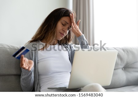 Millennial woman sit on sofa feels stressed using laptop holding plastic credit card having access problem to e-banking service, wrong or forgot password, fraud and scam, cyber criminal victim concept Royalty-Free Stock Photo #1569483040