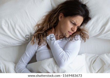 Above view frown millennial woman feels pain in neck after night, awaken in bad temper having painful sudden ache or stiffness, concept of poor incorrect posture during sleeping or too soft mattress Royalty-Free Stock Photo #1569483673
