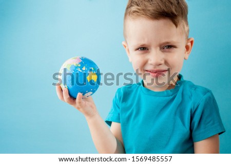 Little boy holding a globe on blue background.