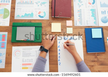 Flat lay background of young woman writing to do list while planning work project sitting at wooden desk, copy space