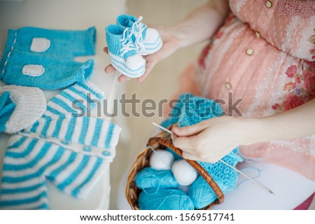 Pregnant woman knits baby clothes on the needles. Booties in the hands.