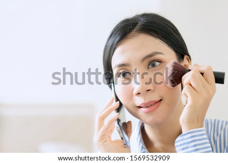 Beautiful Asian businesswoman holding a blush brush while talking on the phone getting ready for work
