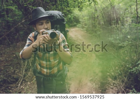 man traveler with backpack using camera to take a photo in the natural forest