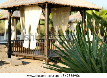 Side view of a wooden gazebo from the sun with curtains on the beach. Recreation areas on the beach. Horizontal, cropped shot, close-up, side view. The concept of recreation and tourism.