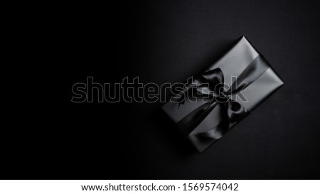 Top view of black gift box with black ribbons isolated on black background. Shopping concept boxing day and black Friday sale composition.