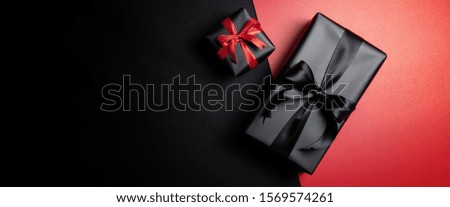Top view of black gift box with red and black ribbons isolated on red and black background. Shopping concept boxing day and black Friday sale composition.