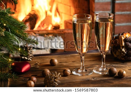 Christmas composition - Two glasses with champagne on a wooden table near a Christmas tree in a room with a burning fireplace