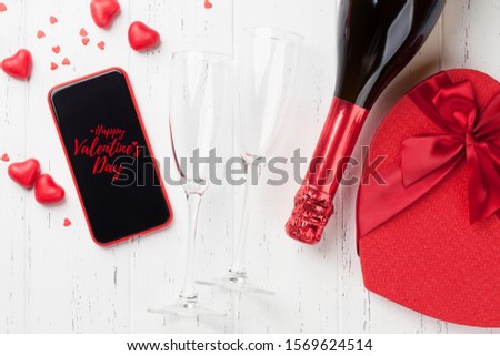 Valentine's day greeting card with gift box, champagne and smartphone on wooden background. Top view with space for your greetings or smart phone app. Flat lay