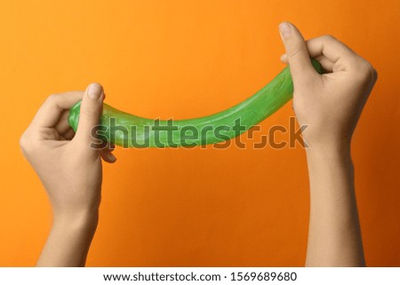 Woman playing with green slime on orange background, closeup. Antistress toy