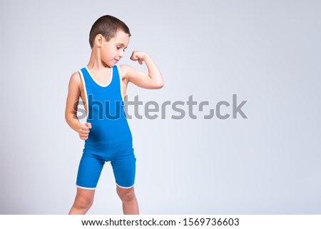 Portrait of a little cheerful boy in a blue  wrestling tights shows biceps, looks confidently at him and poses on a white isolated background. The concept of a little fighter athlete