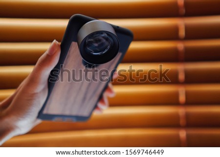 Photo equipment for mobile photography. lens for smartphone. Woman’s hand is handling a phone in wooden case.