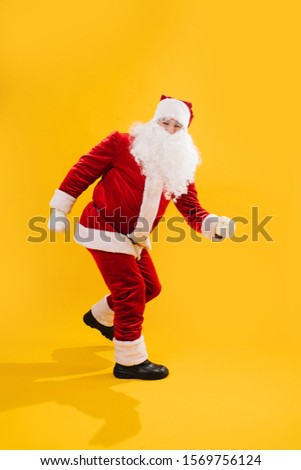 Happy dancing Santa Claus doing a version twist dance, turning from side to side, making moves with arms and legs. Over yellow background. Looking at camera.
