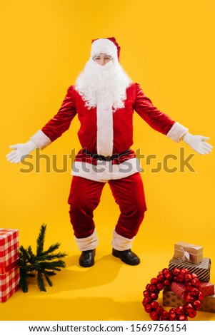 Happy dancing Santa Claus squating with hands and knees apart. He's performing moves from original native dance. Over yellow background. Looking at camera.