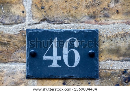 House number 46 on a slate sign on a brick wall