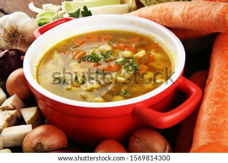 Broth with noodle and carrots, onions various fresh vegetables in a pot - colorful fresh clear spring soup. Rural kitchen scenery vegetarian bouillon or stock