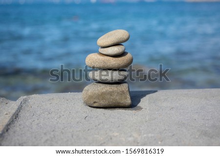 Five stones cairn tower, rock zen sculpture, brown beige pebbles and sea light blue background in sunlight
