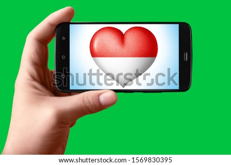 Monaco flag in the shape of a heart on the phone screen. Smartphone in hand shows the heart of the flag on the background hromakey. Object for installation and design.