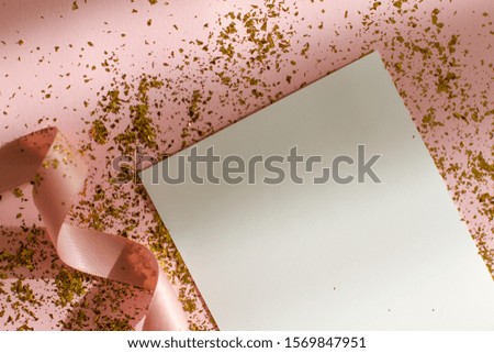 small gold sequins are scattered on a pink background with a pink ribbon and a white leaf. background with beautiful shadow.space for your text. holiday. Christmas, birthday.